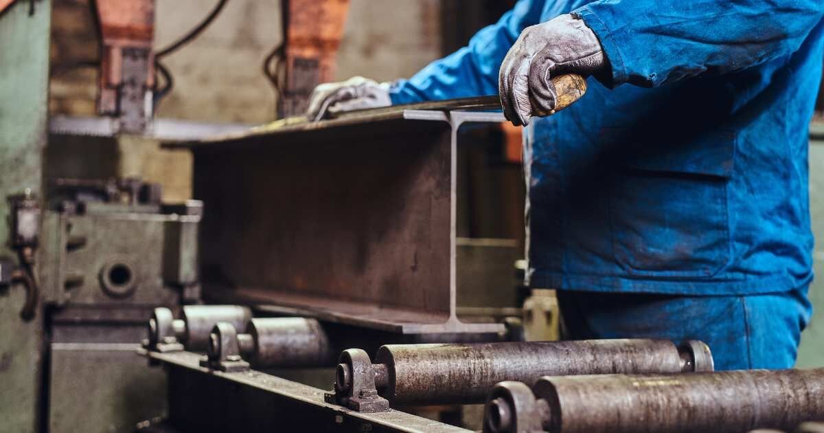 Close-up of a worker handling and measuring a metal beam in a factory setting.